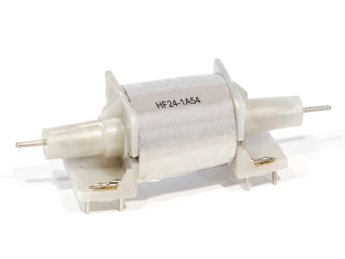 A cylindrical Reed Relay with metal pins on both ends, mounted on a white plastic base. The label HF24-1A54 identifies it as part of the HF Series. by Standex Detect