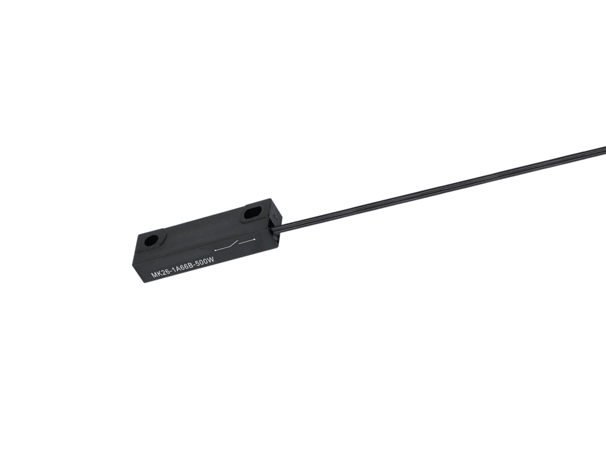 A black, rectangular MK26 Series Reed Sensor with two mounting holes and an attached black cable extending to the right. The sensor features white text labeling on its surface. The background is plain white. by Standex Detect